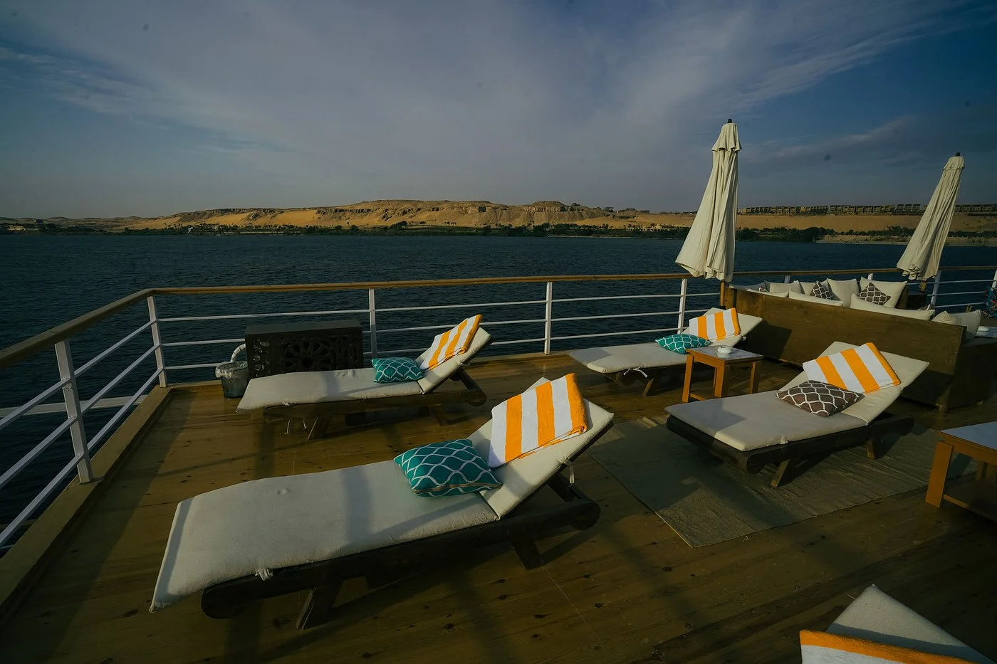 Luxury sun deck of Soul of the Nile Dahabiya with sun loungers overlooking the Nile West Bank dunes