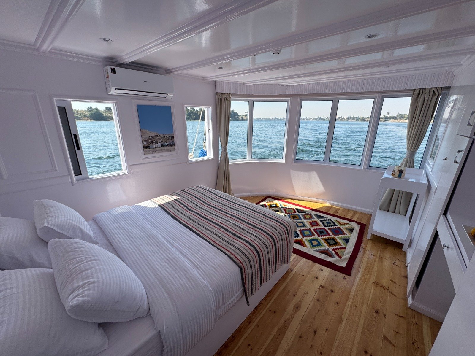 Luxury Panoramic Suite interior on Soul of the Nile Dahabiya featuring a King bed and curved wall-to-wall windows overlooking the river